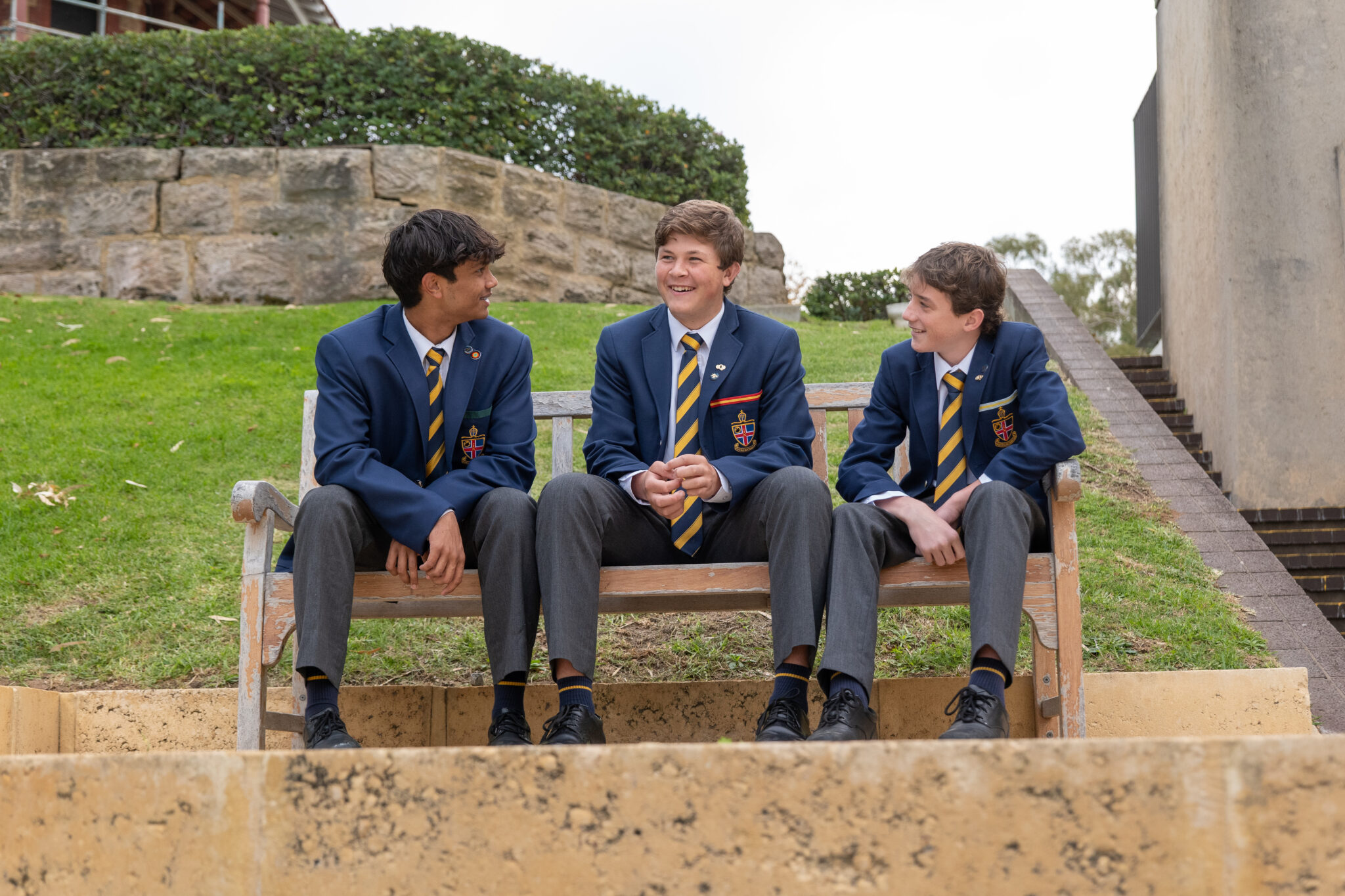 Three boarding students sit on a bench speaking and laughing with each other