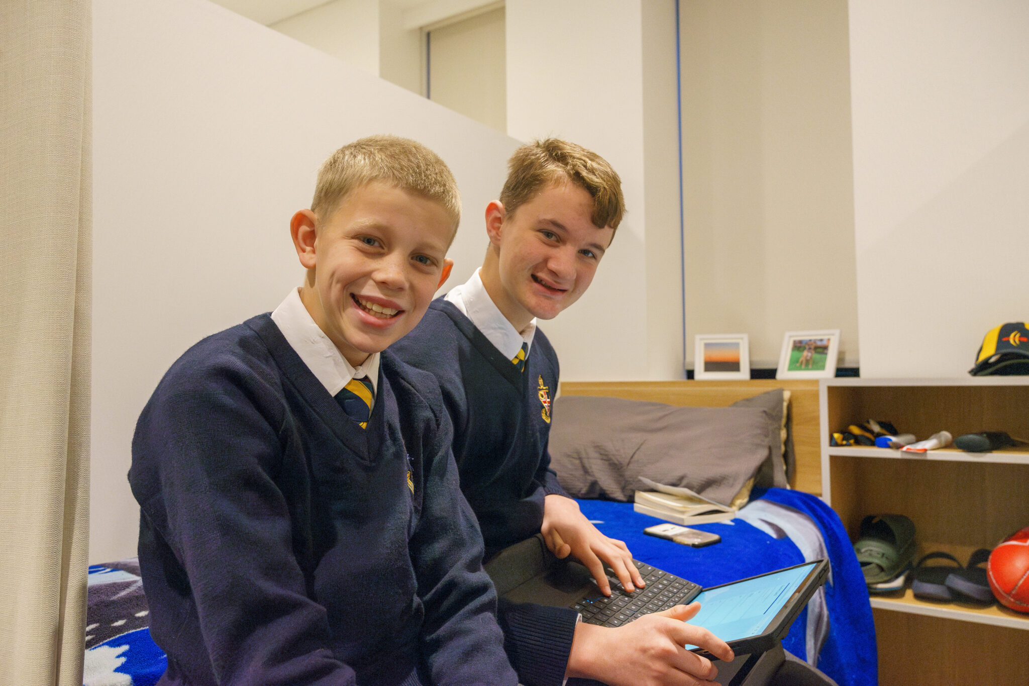 Two boarders seated on a bed, one with a laptop on their lap