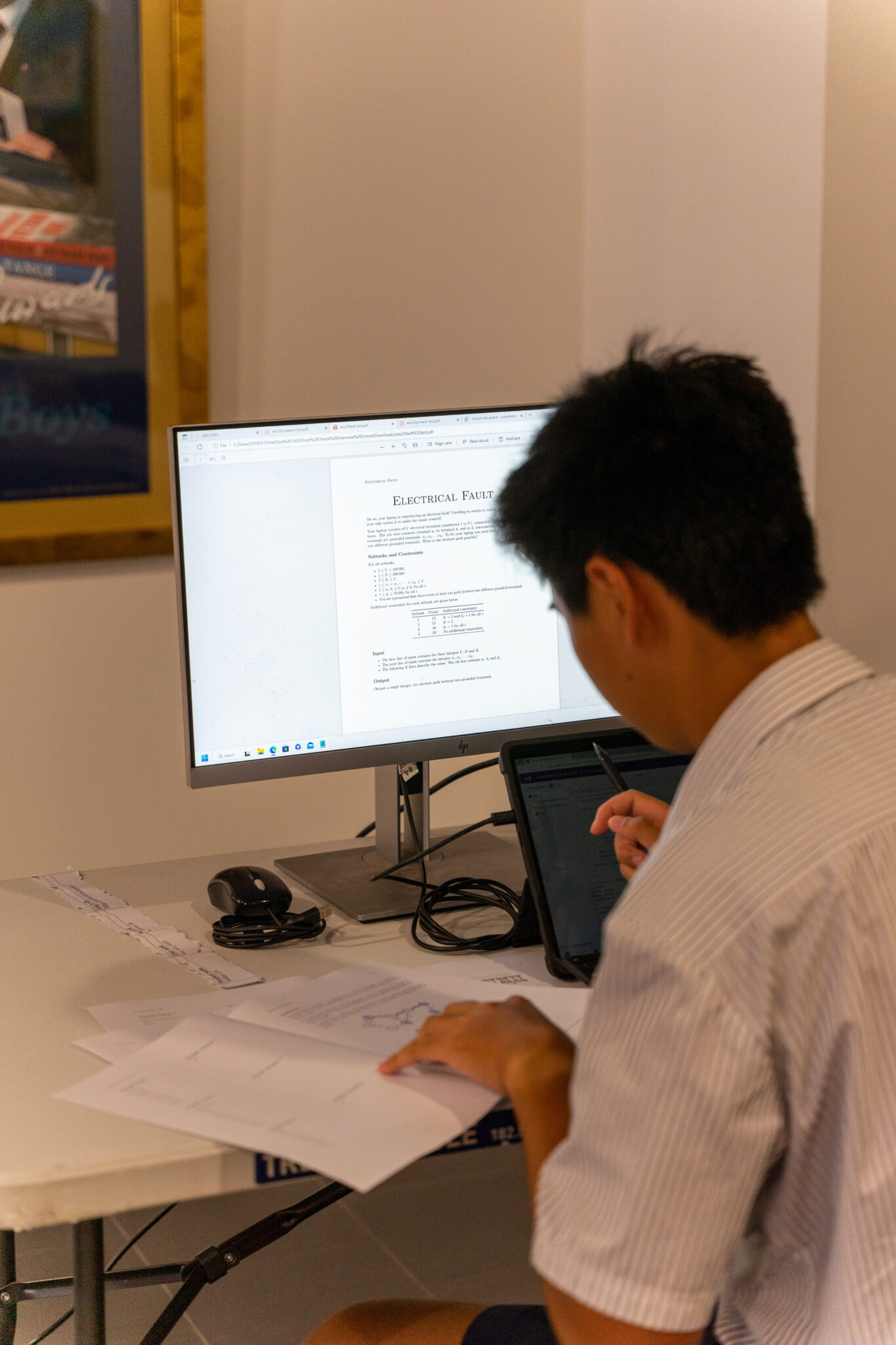 A student sitting behind a computer sceen writing notes while competing in an informatics competition