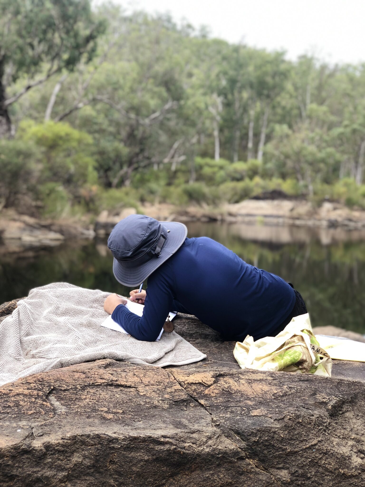 Student writing on the river edge at Kooringal