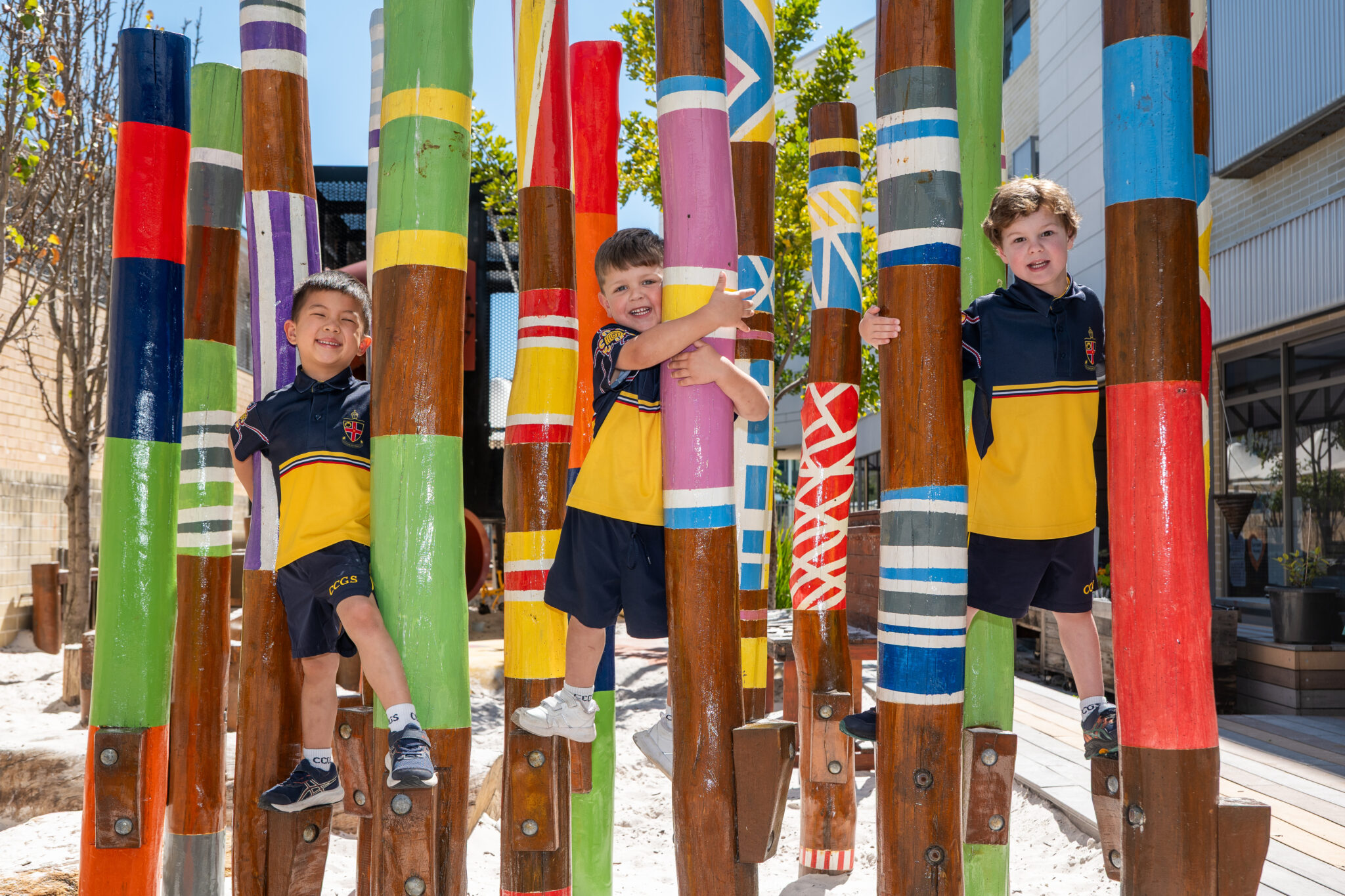 Three Early Learning Community students balancing on totem poles in the ELC playground