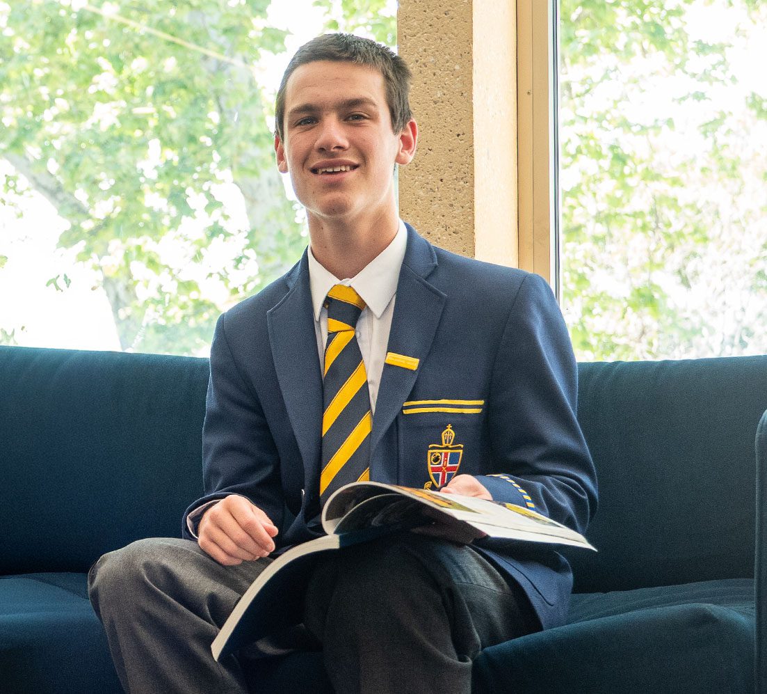 A student smiling while holding the annual yearbook, The Mitre.